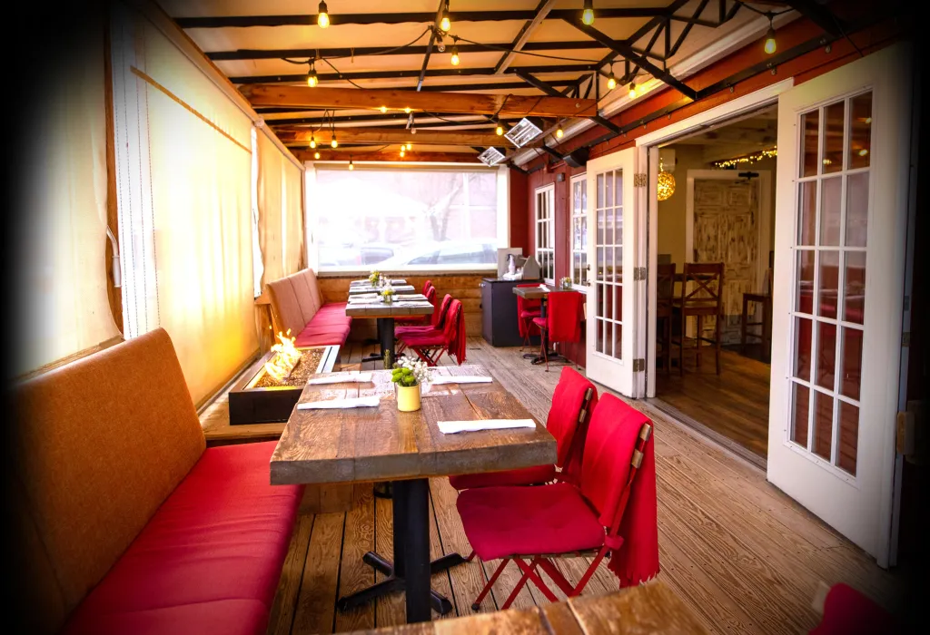 The covered patio dining room at South Lane Bistro, with a fire table and red chairs